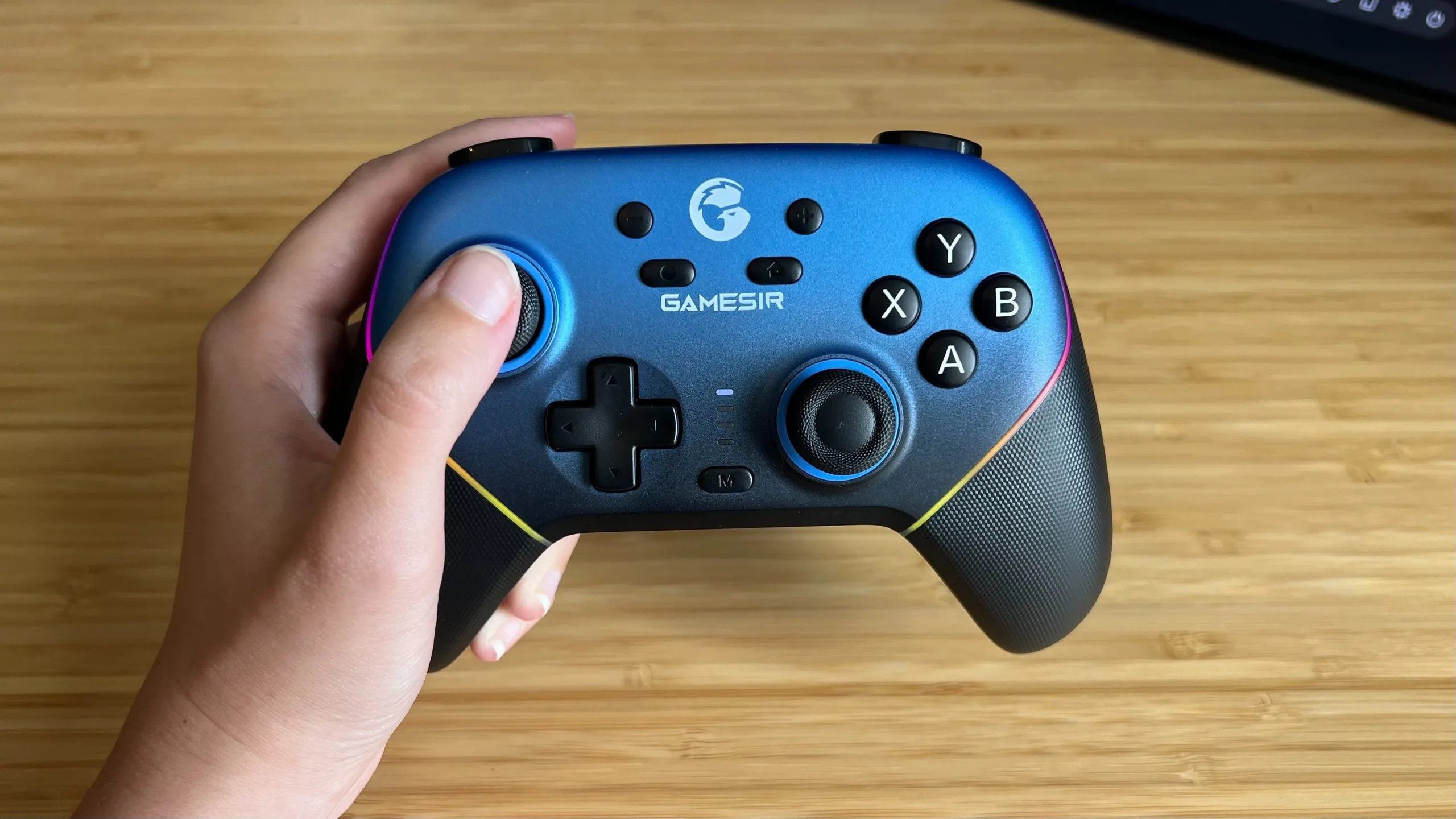 Hand holding GameSir Super Nova controller over a wooden desk