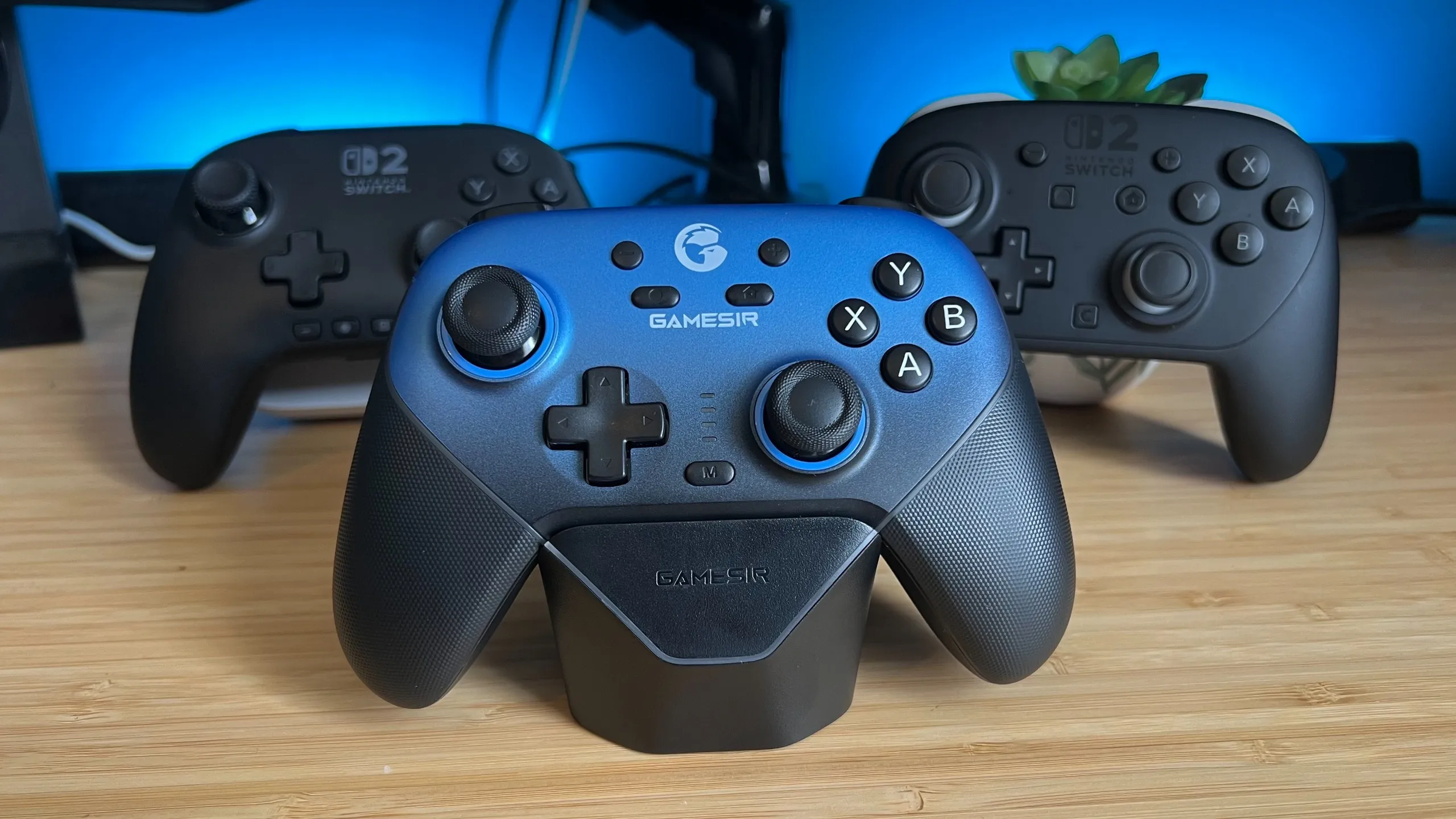 GameSir Super Nova controller on a wooden desk with PowerA Advantage Wired Controller and Nintendo Switch 2 Pro Controller behind it
