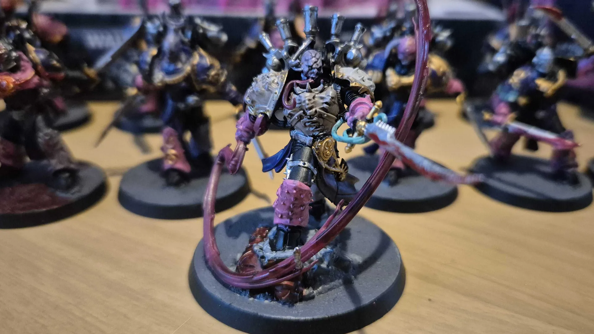 Lucius the Eternal miniature surrounded by other Warhammer Emperor's Children troops, all on a wooden surface