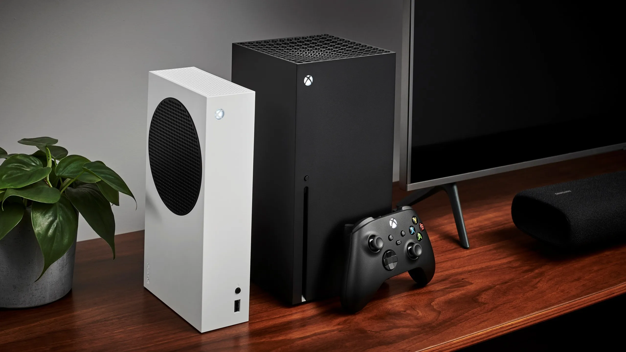 Living room with a pair of Microsoft home video game consoles, including an Xbox Series S (L) and Xbox Series X, alongside a television and soundbar.